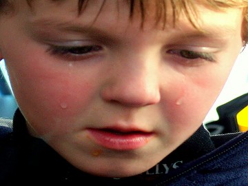 A small boy has a sad expression on his face with tears streaming down his face.