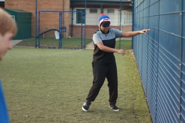 This is a photo of a Bournemouth University student touching a fence on an artificial grass pitch. She is trying to get her bearings as she is blindfolded. She was taking part in a blind football taster session.