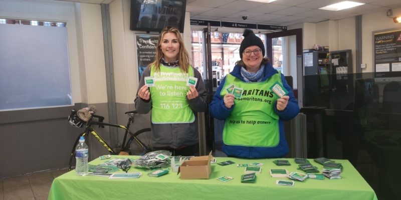 Two Samaritans standing over a table at Bournemouth Train Station
