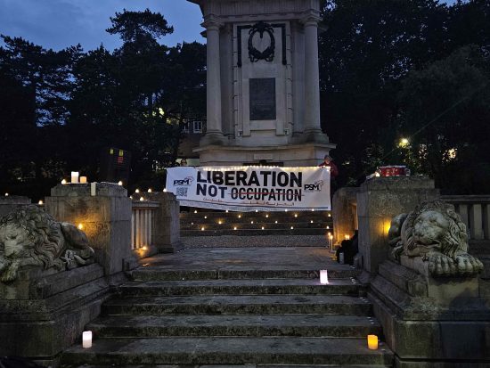 A 'Liberation not Occupation' banner held up at Bournemouth War Memorial. There are several candles surrounding it.