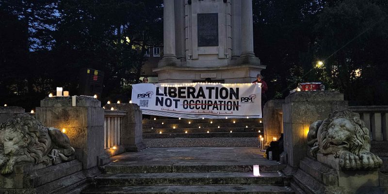 A 'Liberation not Occupation' banner held up at Bournemouth War Memorial. There are several candles surrounding it.