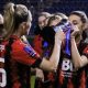 Kelly Fripp helping Maisy Smith drink out of the Hampshire FA Cup. They are both wearing the Bournemouth home shirt.