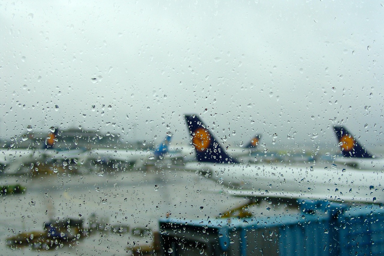 Plane in an airport gate with rain on the window and grey skies.